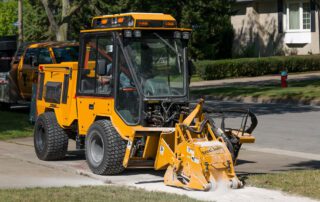 Trackless MT7 sidewalk tractor with cold planer attachment grinding sidewalk