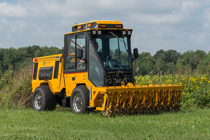 trackless vehicles aerator attachment on sidewalk municipal tractor in field front side view