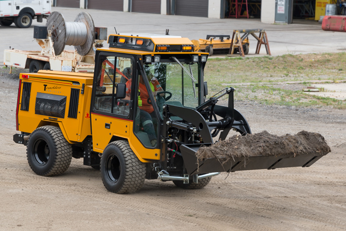 trackless vehicles front end loader attachment on sidewalk municipal tractor carrying dirt